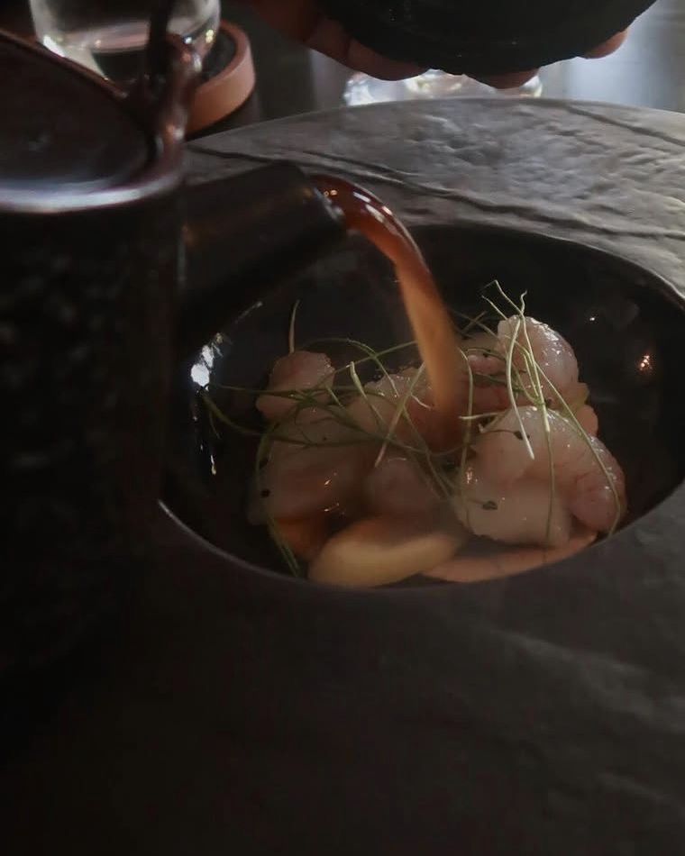 Broth poured over shrimp in a dark stoneware bowl at Ode to Gillian