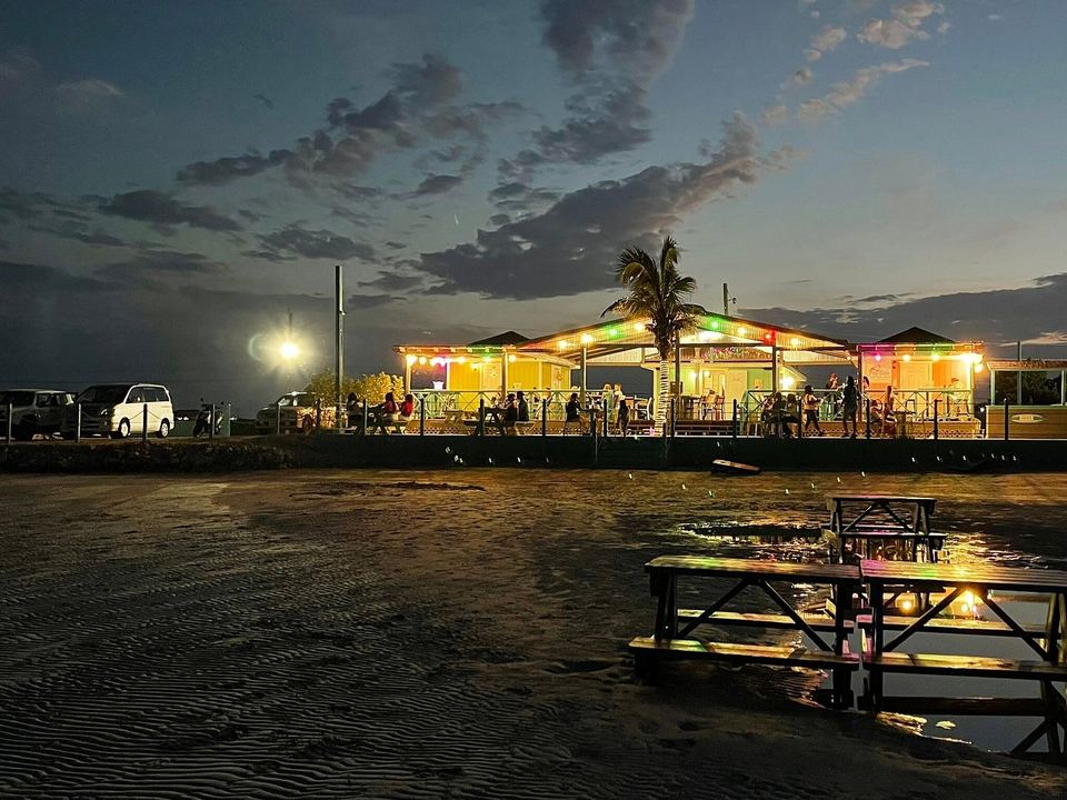 Omar's Beach Hut lit up at dusk, seen across Five Cays Beach at low tide