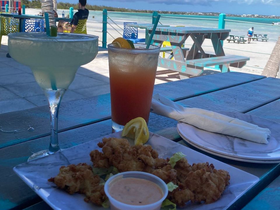 Cocktails and conch fritters on the deck at Omar's Beach Hut, with palms and the beach behind