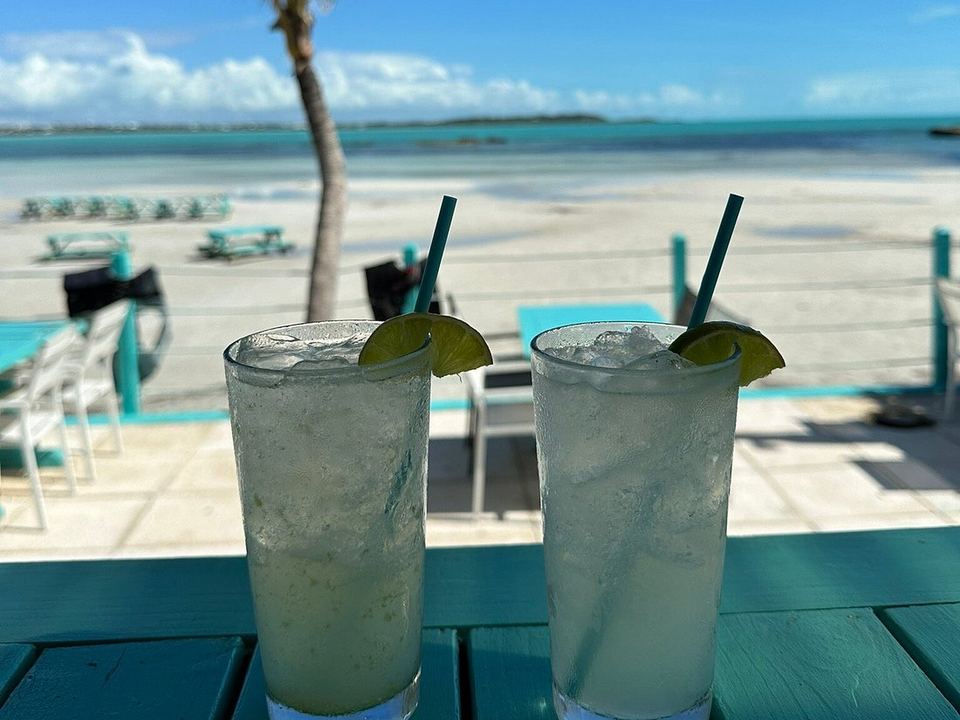 Two iced drinks with lime on the deck at Omar's Beach Hut, with a palm and the beach behind
