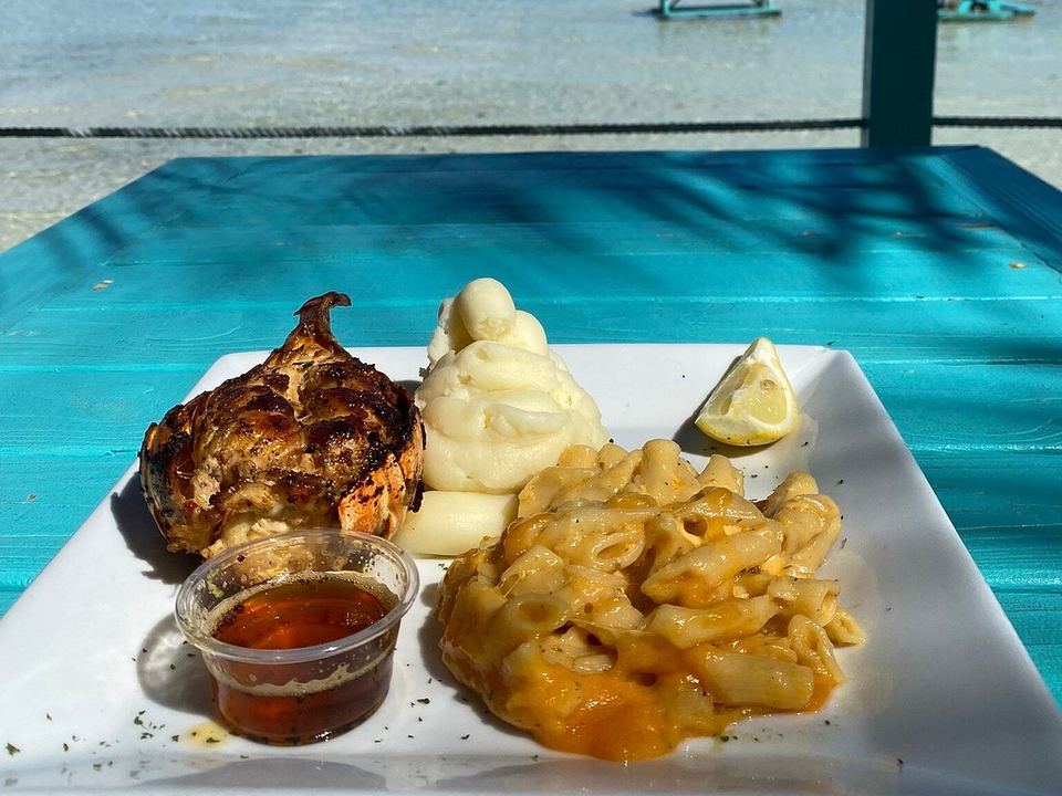 Lobster tail with mashed potato and mac and cheese on a table above the water at Omar's Beach Hut
