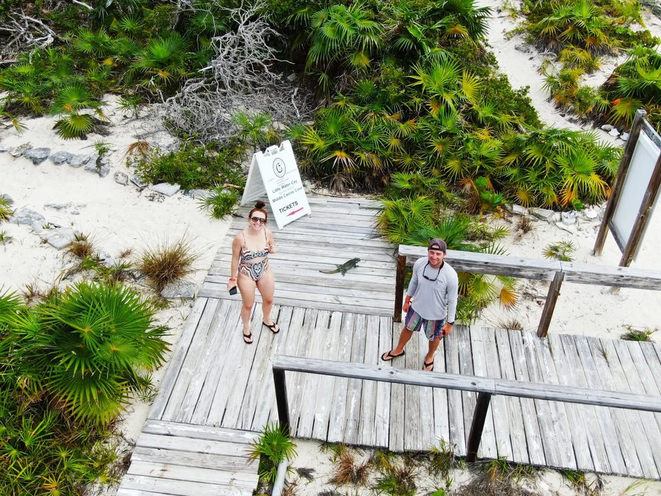 Two visitors on a boardwalk through the dunes, with a rock iguana on the boards beside them