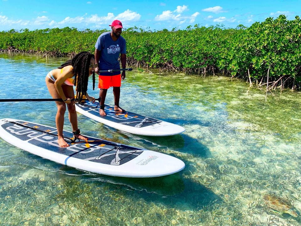 A guide helps a guest find her balance on a paddleboard in a clear channel lined with mangroves