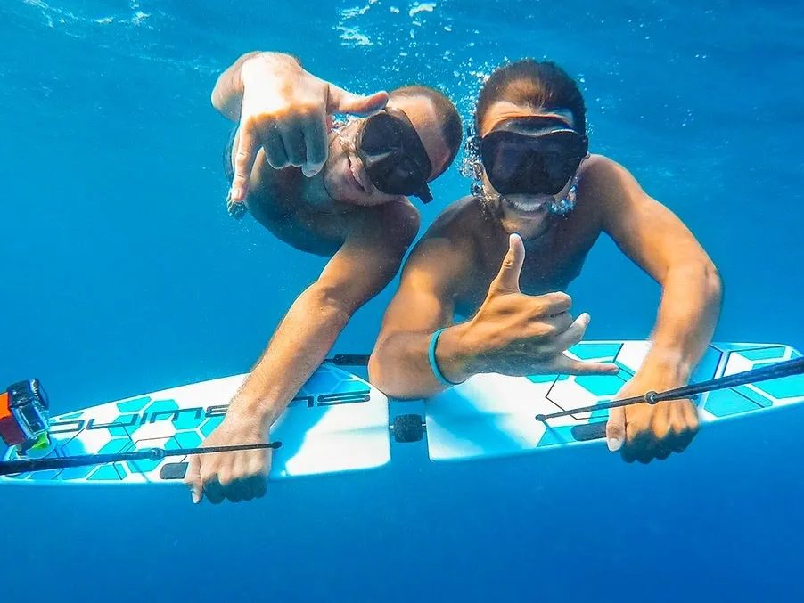 Two guests in masks gliding underwater on a subwing towed behind the boat