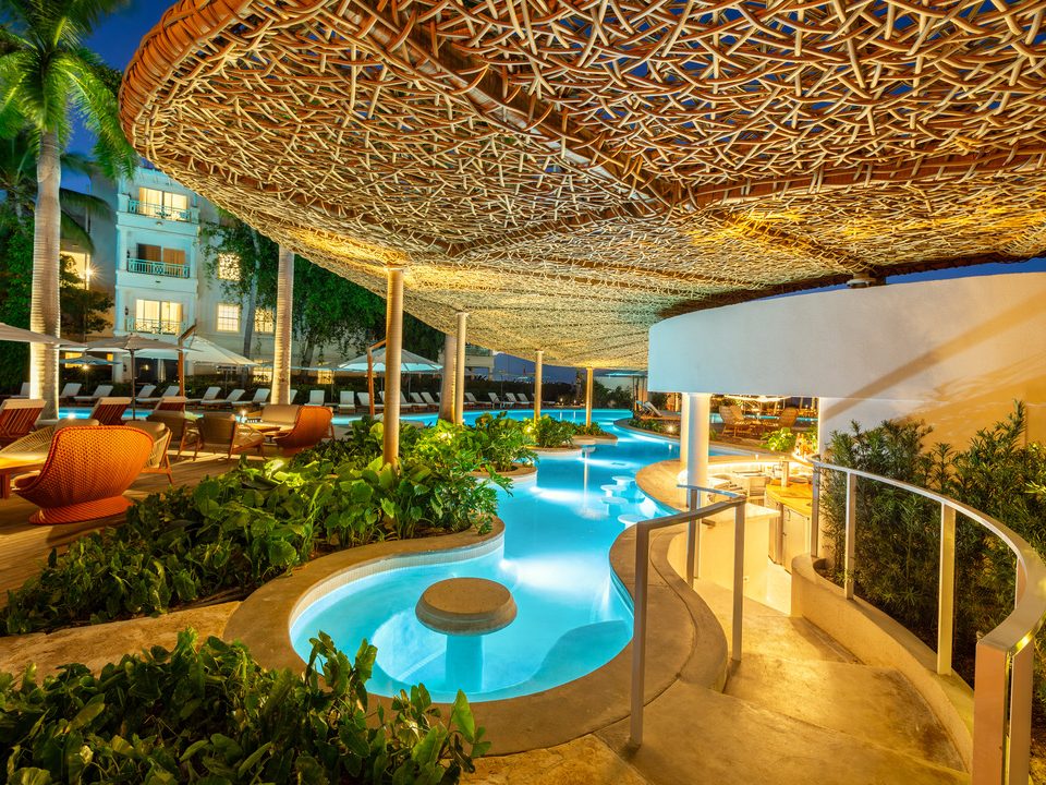 The winding pool lit up at night under the woven canopy