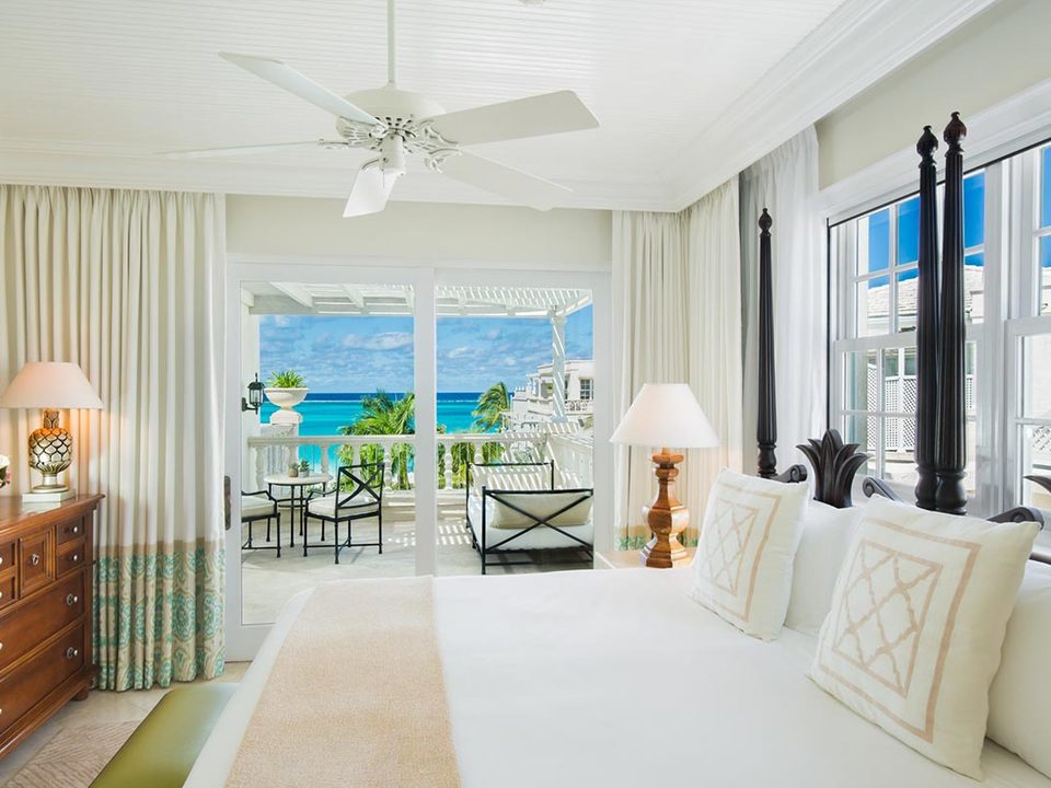 A bedroom with a four-poster bed and a balcony over the sea