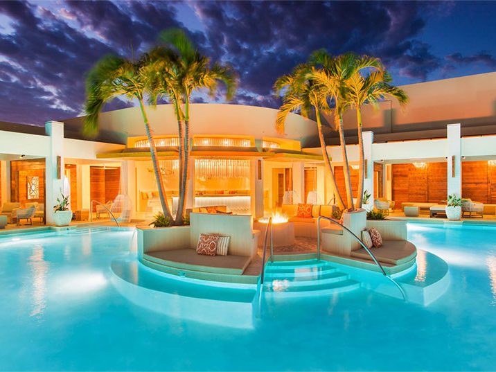 The Colonnade Pool lit up at dusk, with the cabanas behind