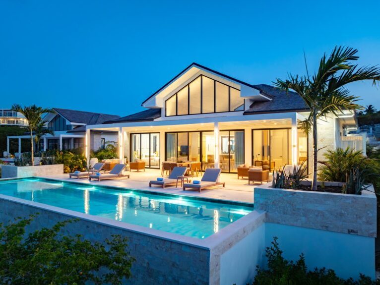 A villa's pool and glass walls glowing at night