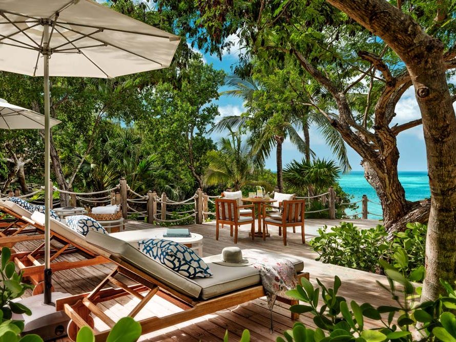 A shaded deck with loungers and a table among the trees, above the sea