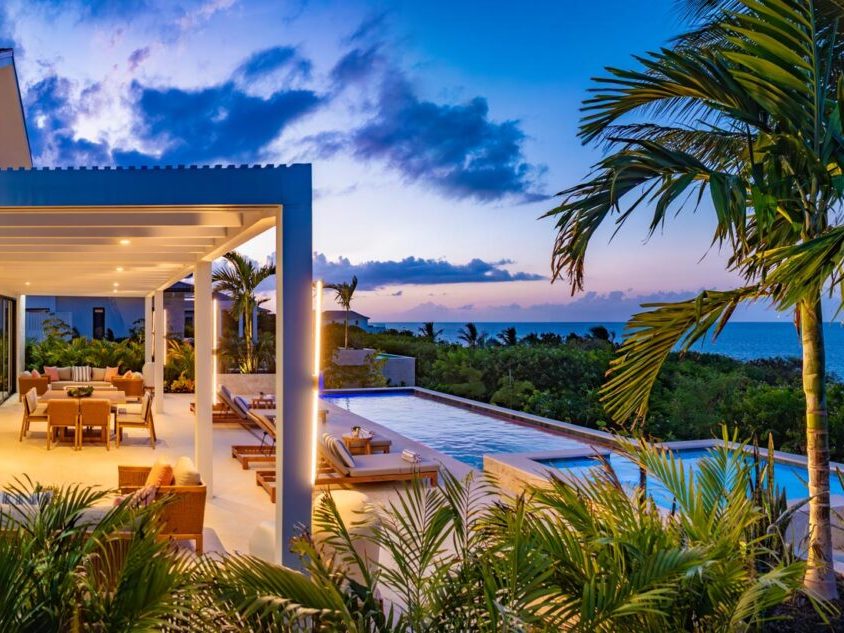 A villa terrace and pool lit up at dusk, with the sea beyond the palms
